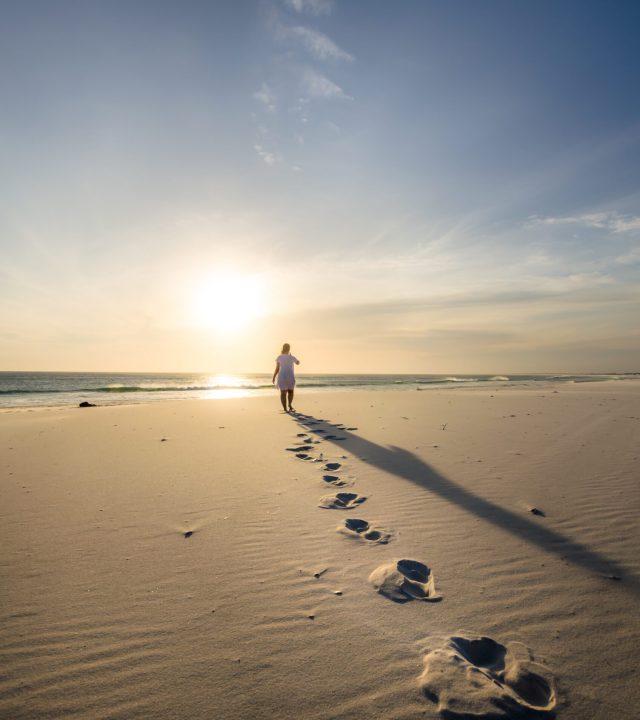 vertical shot of a person walking on the sandy beach with footsteps on the foreground